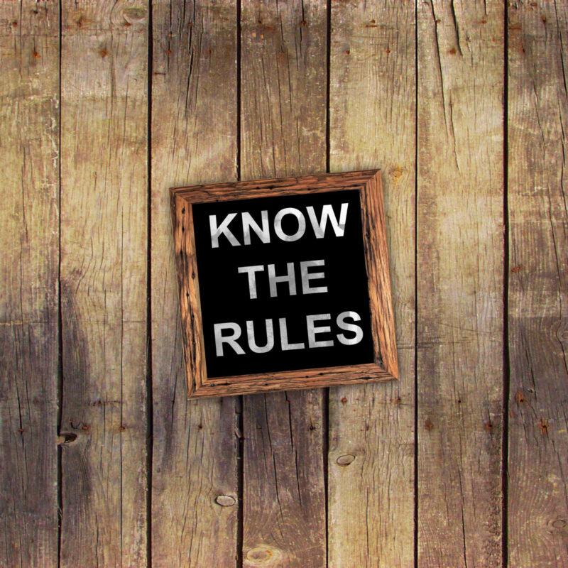 ύλινος τοίχος με πινακίδα σε κορνίζα που γράφει 'KNOW THE RULES' με λευκά κεφαλαία γράμματα σε μαύρο φόντο.