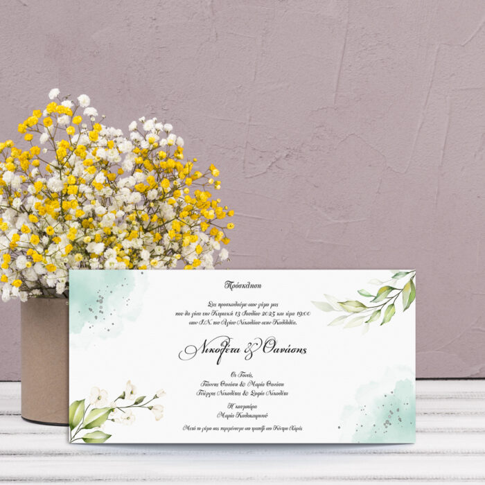 Greenery Watercolor 200x100 Πρόσκληση γάμου με πράσινα φύλλα και λευκά λουλούδια σε τετράγωνο σχήμα, μπροστά από βάζο με λουλούδια.